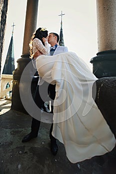 Fiance holds bride in his arms on the rooftop of old cathedral