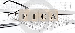 FICA written on wooden cube with keyboard , calculator, chart,glasses.Business concept