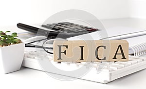 FICA written on a wooden cube on keyboard with office tools