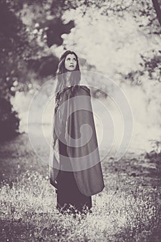 Fiction woman in cloak in forest.