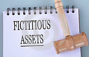 FICTITIOUS ASSETS - words in a notebook on a gray background with a judge\'s gavel photo