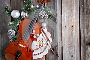 Fiddle and bow adorned with Christmas balls on wood background