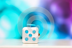 Fidget cube anti stress toy. Detail of finger play toy used for relax. Gadget placed on colorful bokeh background