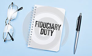 fiduciary duty words in white notepad, pen and glasses on blue background. Concept