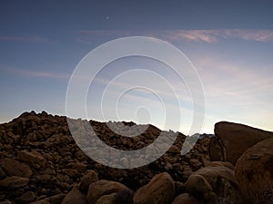 Field of boulders at dusk with sunset sky and crescent moon in Yucca Valley California near Joshua Tree National Park