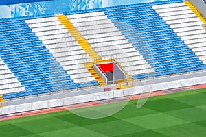 Field of empty white and blue seats, yellow stairs, gate exit on the stadium corner