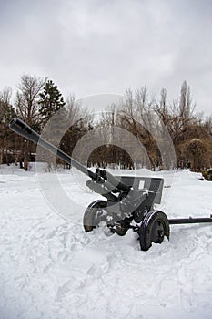 Field gun covered with snow at the edge of a forest 