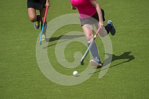 Field hockey player, in possesion of the ball, running over an astroturf pitch, looking for a team mate to pass to