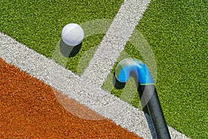 Field hockey stick and ball on brown and green grass