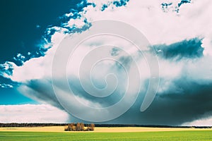 Field Or Meadow Landscape With Green Grass Under Scenic Spring Blue Dramatic Sky With White Fluffy Clouds. Rain Clouds