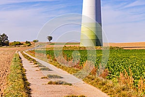 Field path through nature in front of a huge wind turbine tower