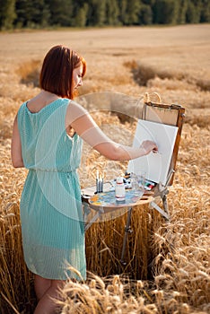 Field of ripe wheat on sunset time, girl artist drawing a picture