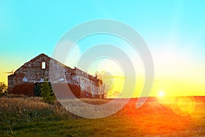 On the field stands an abandoned building of red brick. The bright sun at sunset shines with bright rays radiating glare.