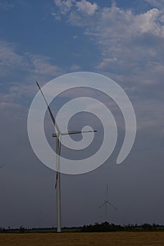 A field of windmills spin in front of a colorful evening sky. A wind turbine is used to produce electricity. Wind energy is the