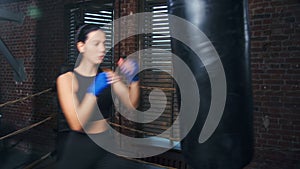 Fierce Asian fit woman with wrapped hands practicing kickboxing on punching bag at box studio