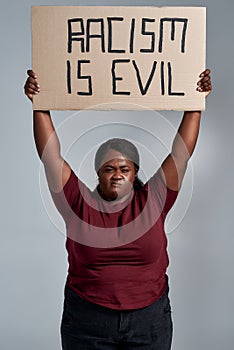 Fierce plus size young african american woman in casual clothes looking at camera, holding Racism is evil banner above