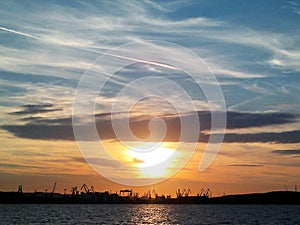 Fiery glow sunset over the Baltic sea water. Different colours of clouds and the silhouette of shipyard in Gdynia City, Poland