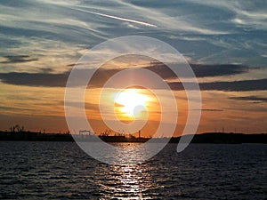 Fiery glow sunset over the Baltic sea water. Different colours of clouds and the silhouette of shipyard in Gdynia City, Poland