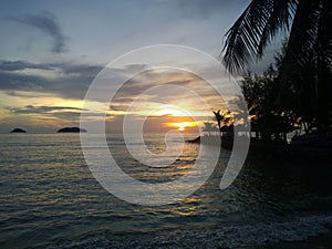 Fiery glow sunset over a beautiful tropical beach and ocean water. Different colours of clouds and the silhouette of palm tree.