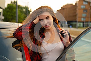 With fiery red locks and a beaming smile, the young woman wearing poses beside red car