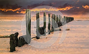 Fiery sunset sky over old water breaker, groyne on a wet sandy b