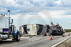 Fifth wheel RV overturned on highway with wench truck trying to get it off the road and two semis parked nearby and traffic cones