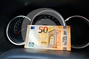 Fifty euro bill in front of the dashboard dials of a car