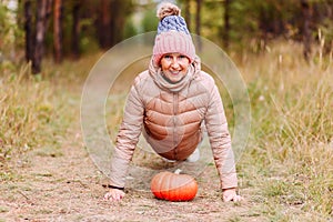 Fifty-year-old beautiful woman in a hat and jacket and orange pumpkin outdoors. harvest in autumn