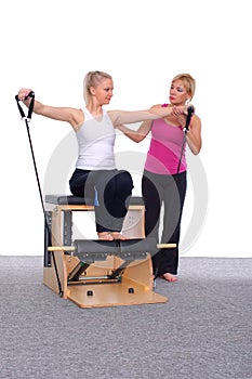 Fifty-year-old trainer teaches Pilates exercises to elevator chair, young girl with help of gymnastic rubber arm muscles