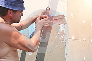 Fifty years old manual worker with wall plastering tools renovating house. Plasterer renovating walls and corners with spatula and