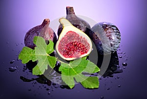 Fig fruits. Ripe sweet figs fruit with leaves close up, on purple, violet background. Water drops