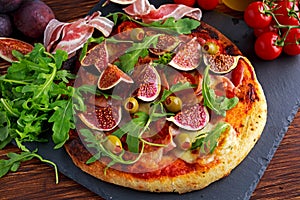 Fig pizza with bacon, green pimiento olives, rocket and basil leaves