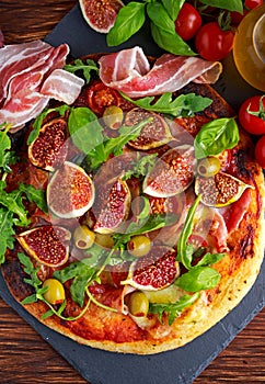 Fig pizza with bacon, green pimiento olives, rocket and basil leaves