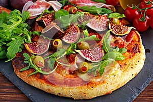 Fig pizza with bacon, green pimiento olives, rocket and basil leaves