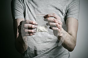 The fight against drugs and drug addiction topic: addict holding package of cocaine in a gray T-shirt on a dark background