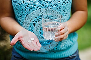 Fight against severe headache, girl holds a glass of clean water and two white pills