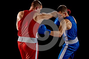 Fight. Dynamic portrait of two professional boxer in sports uniform boxing isolated on dark background. Concept of sport