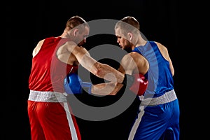 Fight. Dynamic portrait of two professional boxer in sports uniform boxing isolated on dark background. Concept of sport