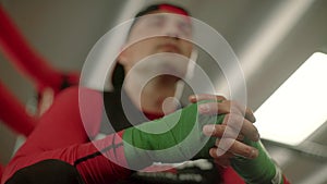 Fighter, boxer putting on hand wraps while sitting on a ring preparing for fight. A look