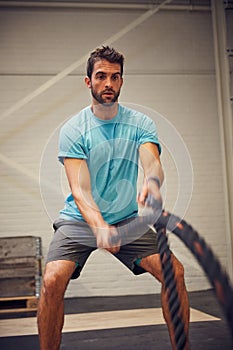 Fighting fit. a handsome young man working out with battle ropes in the gym.