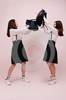 Fighting schoolgirl twins bashing each with their backpacks for fun