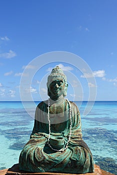 A figure of Buddha in front of a turquoise lagoon on the island of Fakarava in French Polynesia in the South Pacific; copy space photo