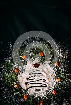 The figure of a Christmas tree made of flour on a black background in a frame made of fir branches