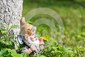 The figure of a garden gnome with a shovel at a tree in the green grass. Close-up. Copy space