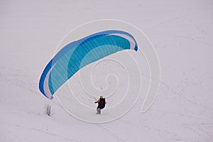 A figure of man with blue paraglider in a snow covered park