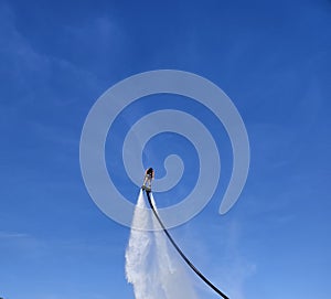 The figure of a man on a flyboard, engaged in hydroflight against the background of a juicy, blue sky