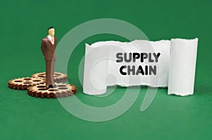 The figure of a man stands on the gears and reads the inscription - SUPPLY CHAIN on paper