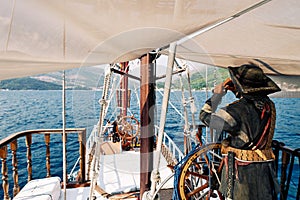 Figure of a pirate with a telescope stands at the helm of a sailboat sailing on the sea. Back view