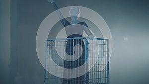 The figure of professional ballerina dancing in black dress in the studio in big blue cage in the black background with