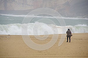 A figure of a woman walking on an empty beach in a storm